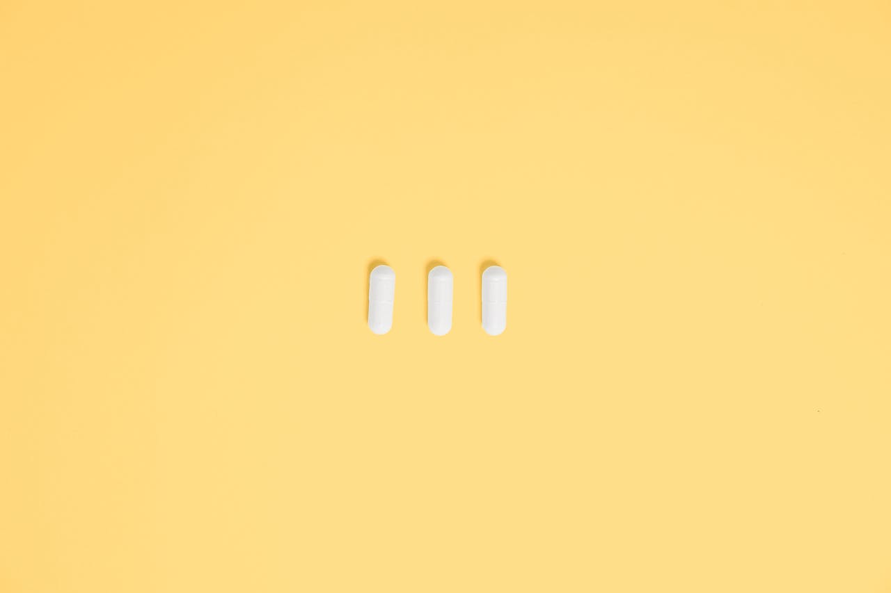 Three white capsules on a vibrant yellow background, symbolizing healthcare and medication.